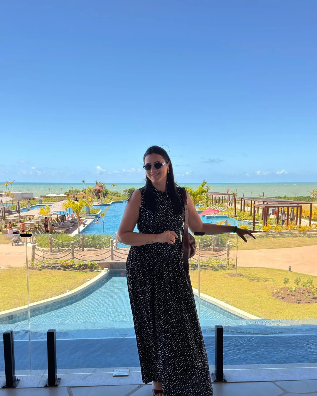 Lanna de vestido preto diante de uma vista de lazer e mar